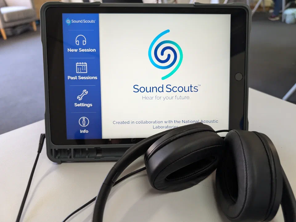 iPad in a stand showing the Sound Scouts app home screen, with a pair of headphones resting in front of it.