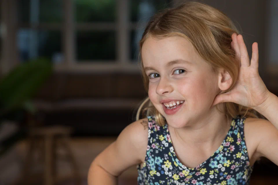 Girl with hand up to ear to listen.