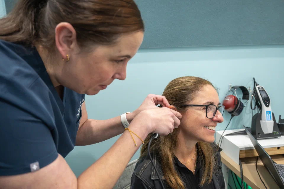 A female audiologist uses an otoscope to examine a woman's ear.