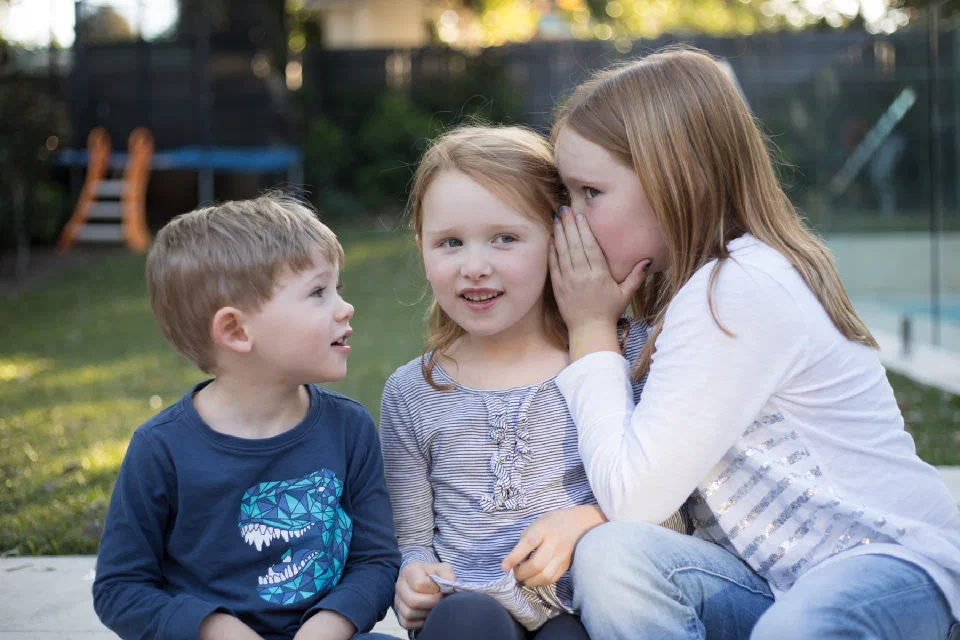 Three children whispering in each others ears.
