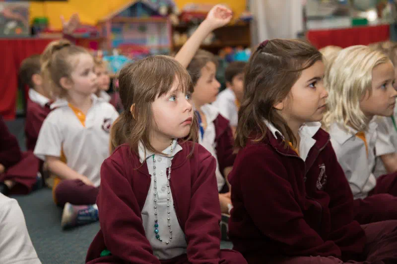 Group of young sitting on the floor of their classroom listening intently.