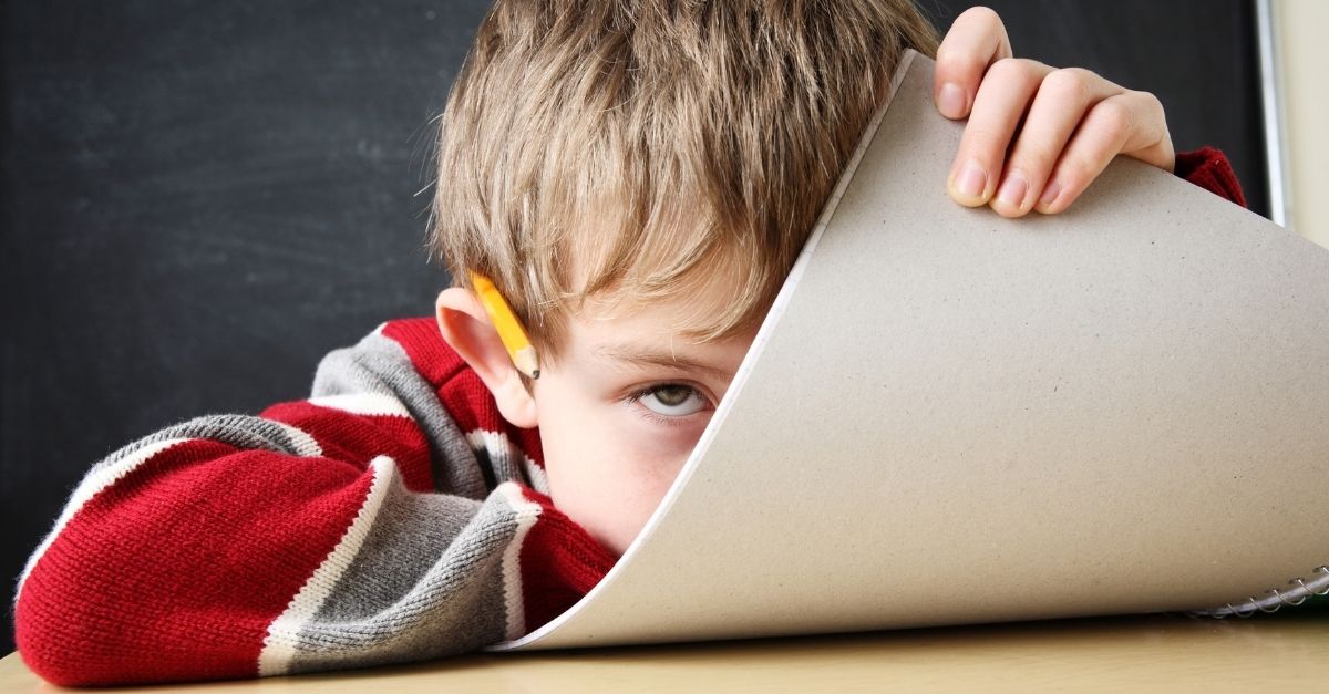 Boy with ADHD sitting in class hiding behind his workbook with pencil in ear