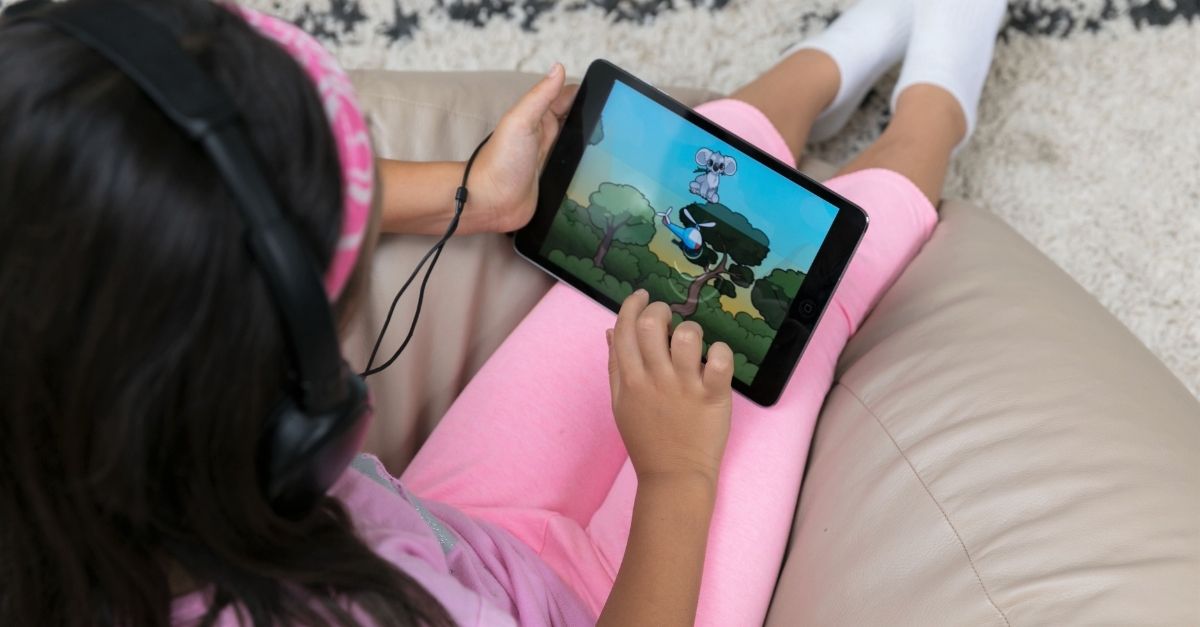 Child sat down on couch in pink pyjamas playing Sound Scouts app on tablet device