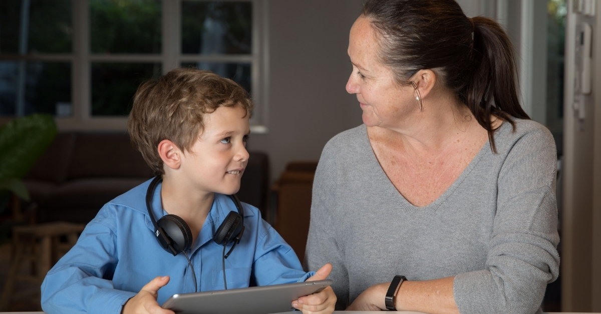 Boy looking up at his mum with iPad in hand and headphones around neck